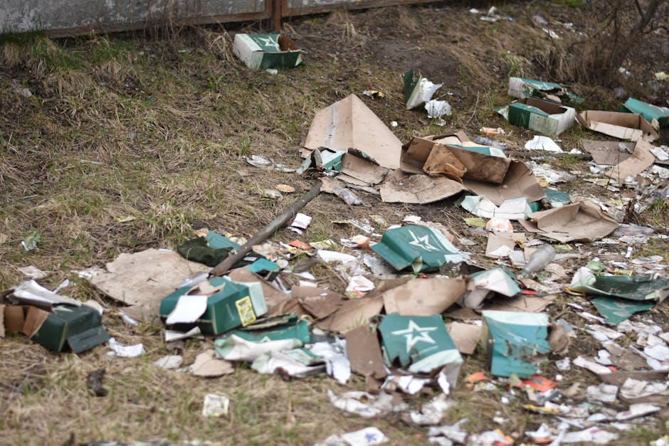 A small blue pickup truck parked alongside a curb on a street, heavily loaded with miscellaneous waste materials. The truck's cargo area is filled with a variety of items, including cardboard boxes, b